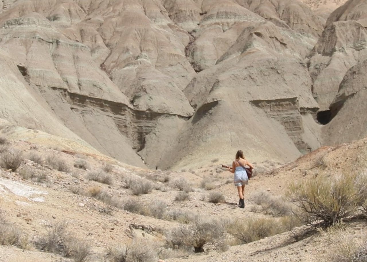 A woman in a white dress playing guitar in the desert.