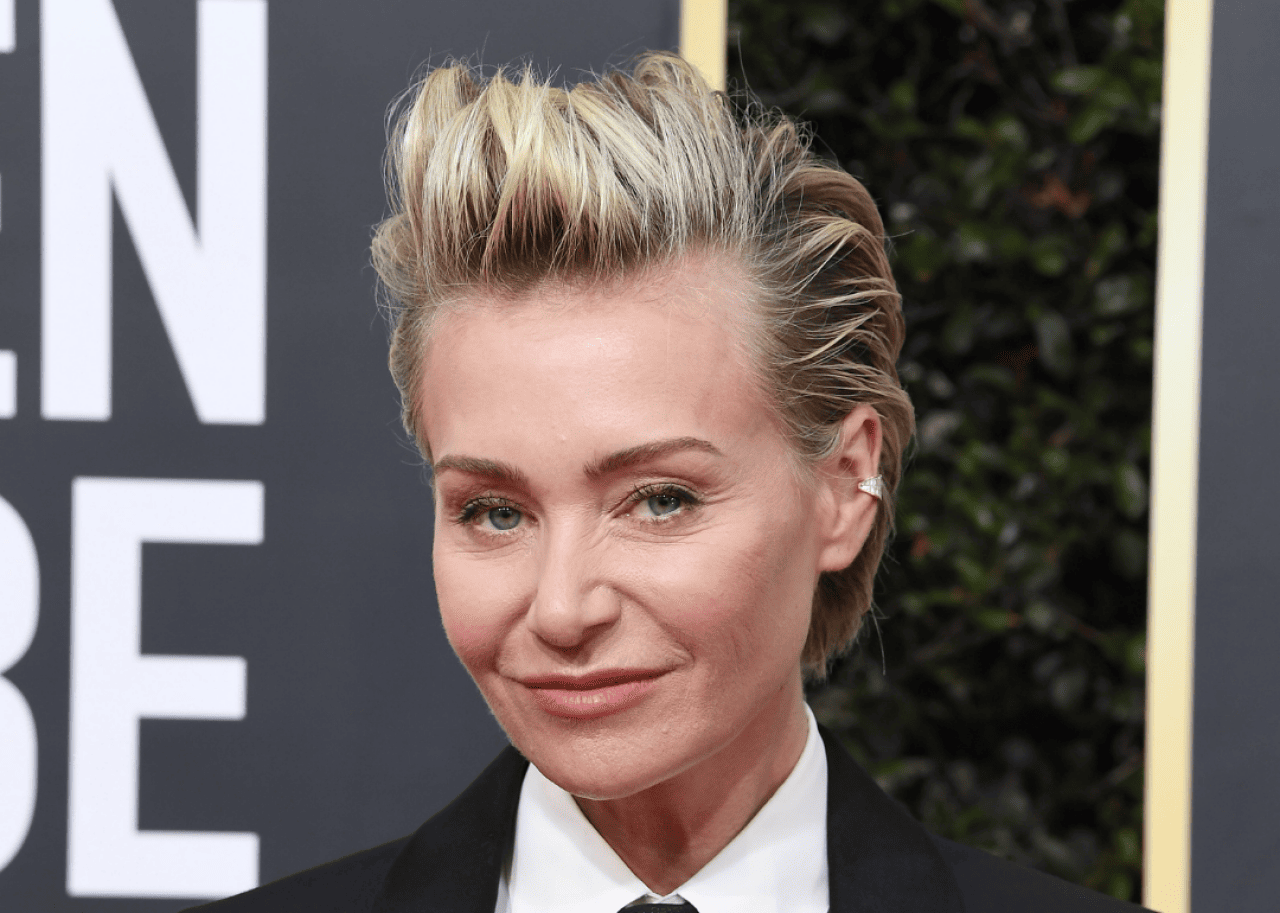 Portia de Rossi smiles wearing a black suit and tie.