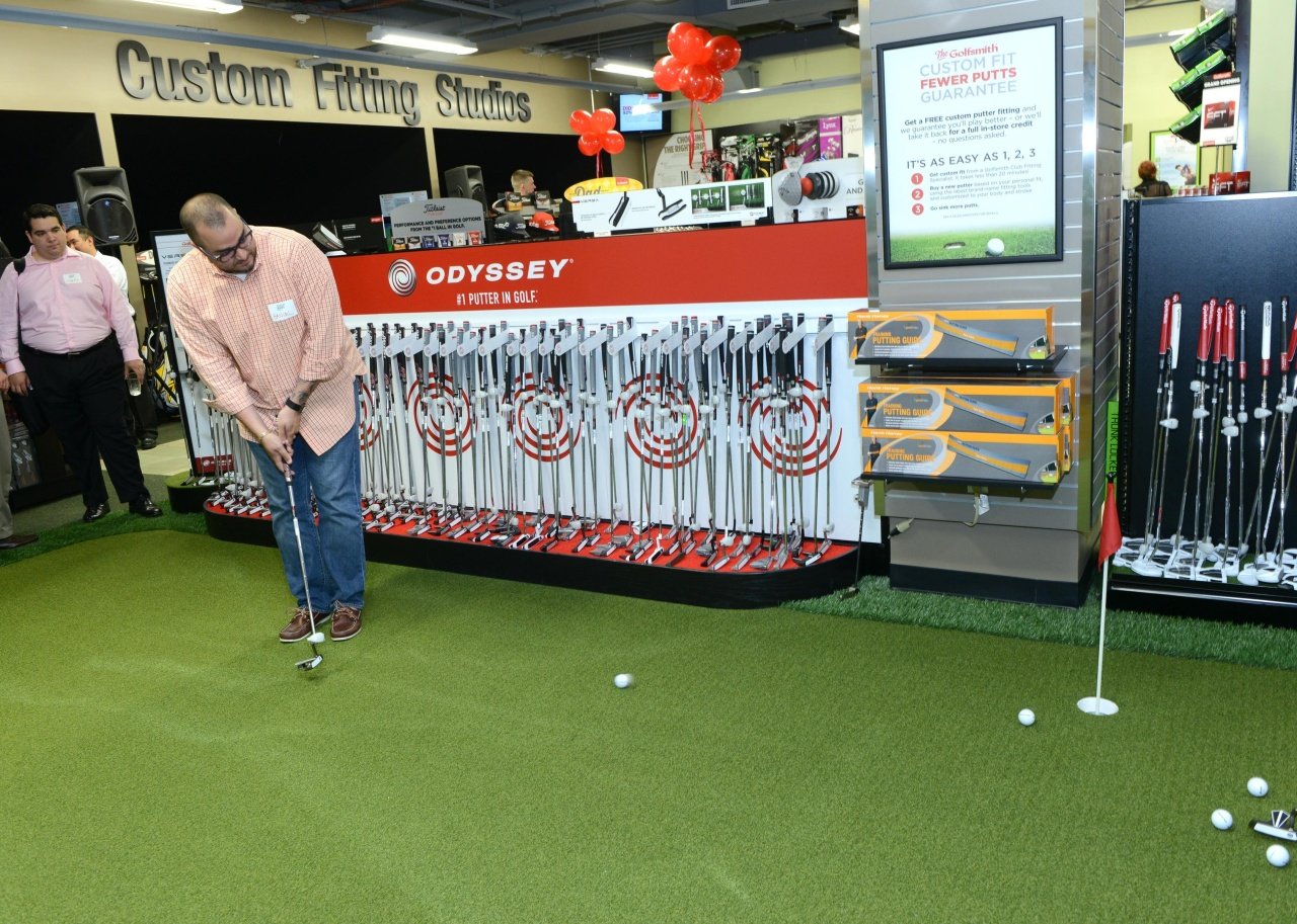 A man putting a golf ball on green turf inside a store.