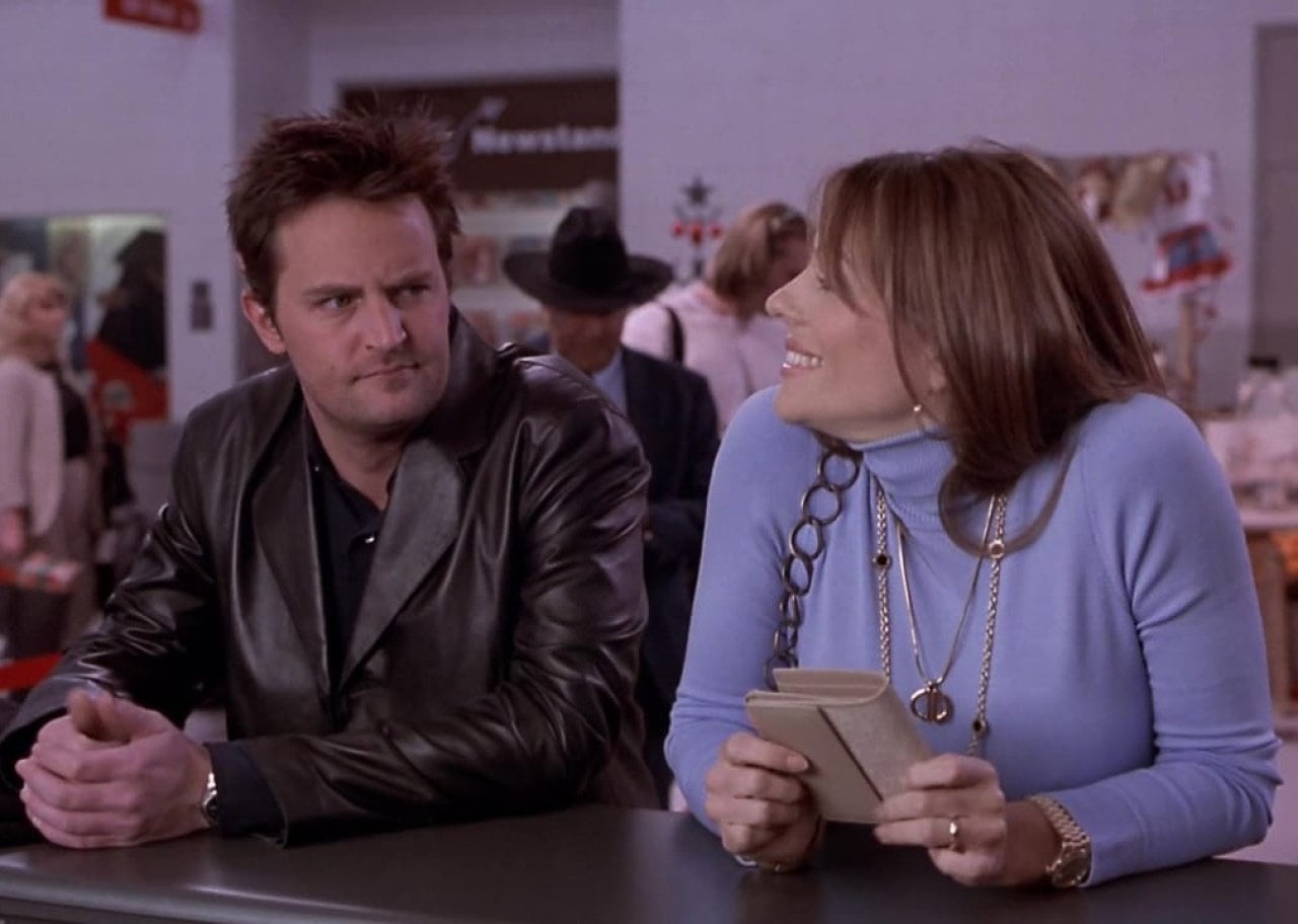 Matthew Parry sitting at a bar talking to Elizabeth Hurley, smiling.