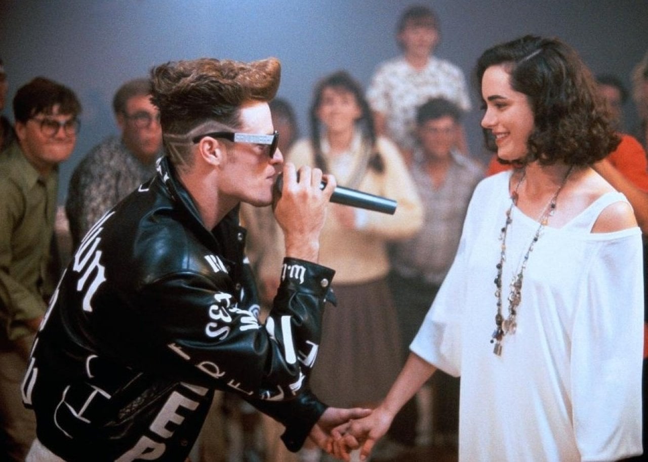 Vanilla Ice in a black and white leather jacket singing to a woman in a white off the shoulder shirt.