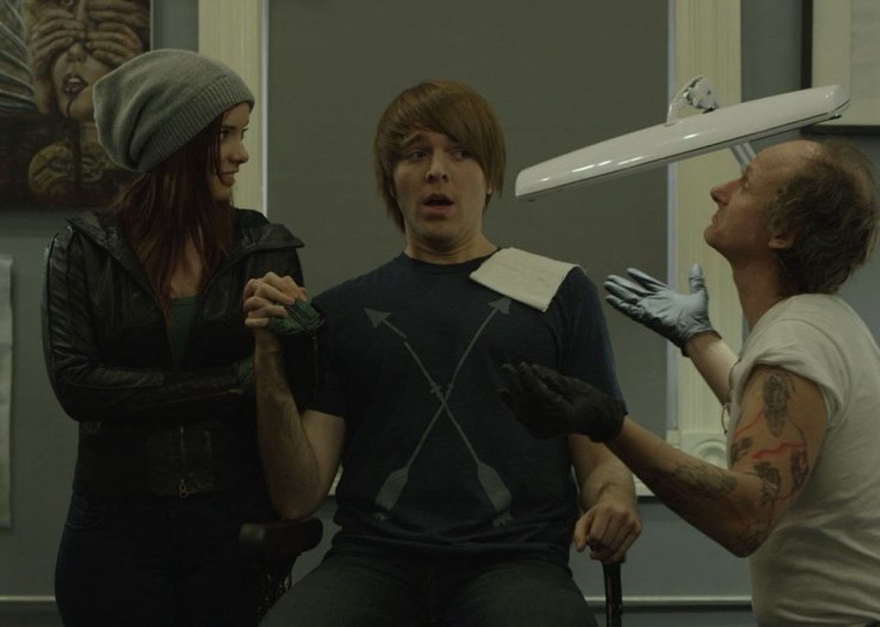 A boy and girl holding hands while a tatoo artist throws his hands in the air.
