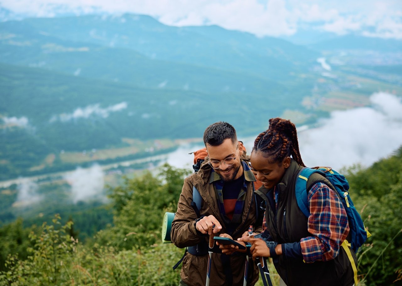 A man and woman looking at a map on mobile phone while hiking.