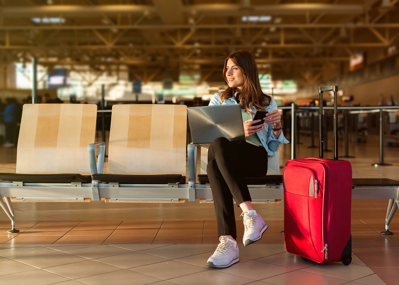 Female passenger on phone and laptop sitting in terminal waiting for her flight.