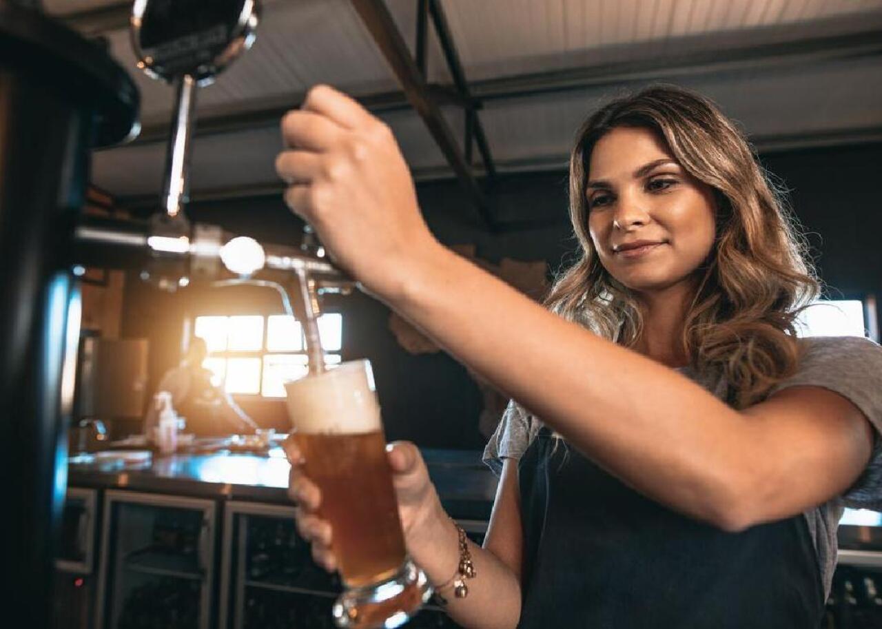 A woman fills a pint glass from a beer tap. 