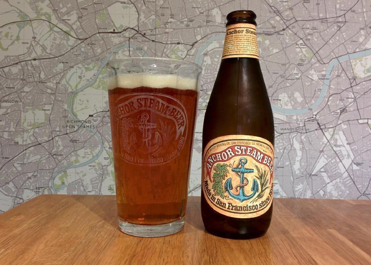A bottle and glass of Anchor Steam beer sit on a table.