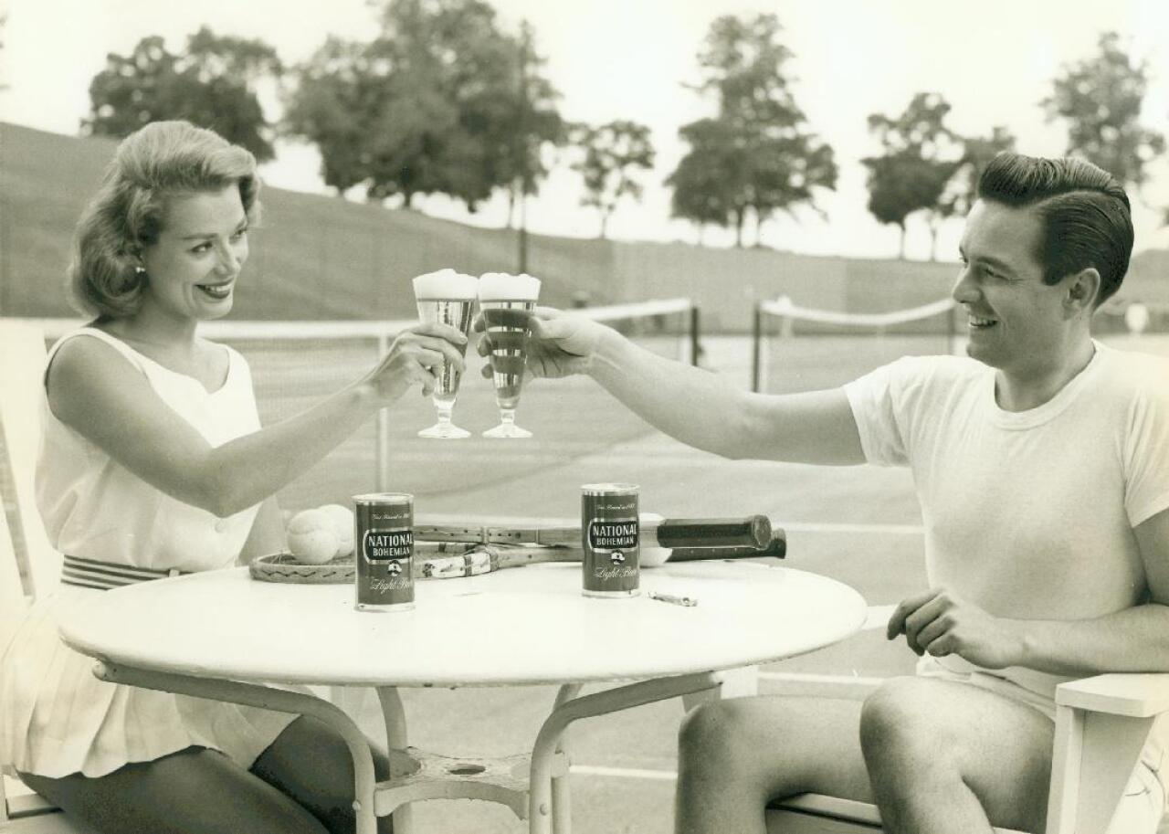 A woman and man raise their glasses in a National Bohemian beer ad.