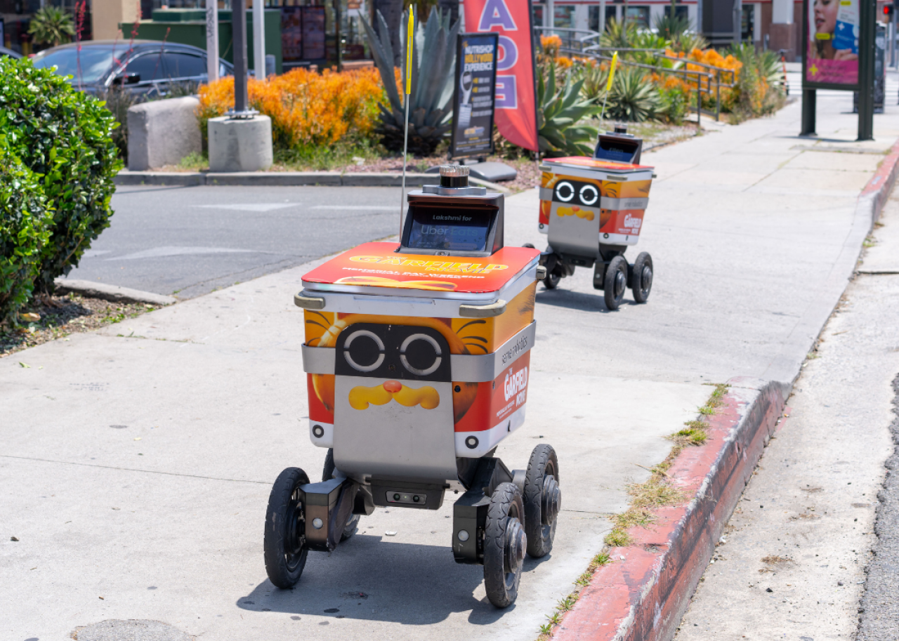 Two delivery robots in the city going down a sidewalk.
