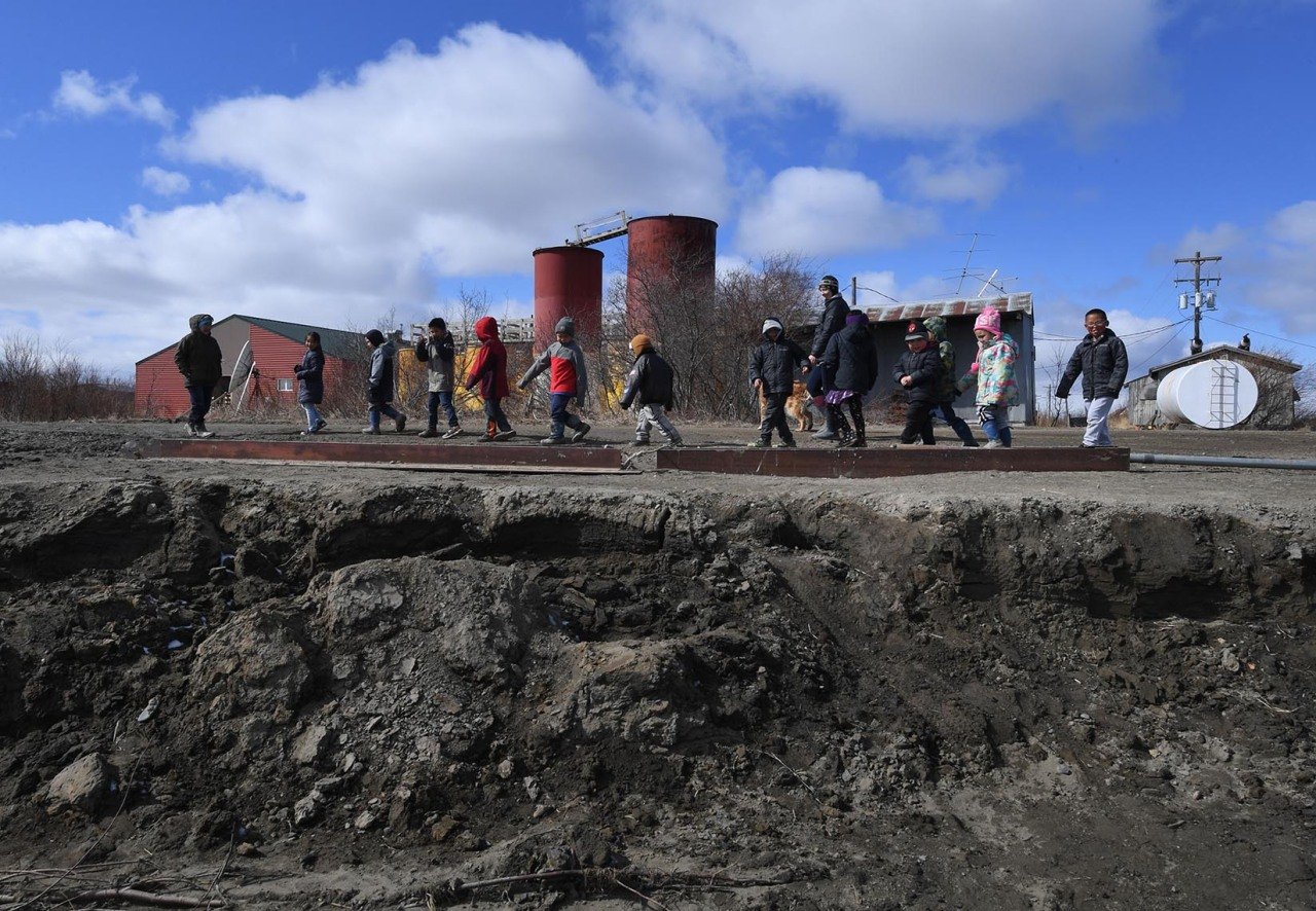 Schoolchildren walk beside severe erosion of the permafrost tundra next to their school at the climate change affected Yupik village of Napakiak on the Yukon Delta in Alaska.