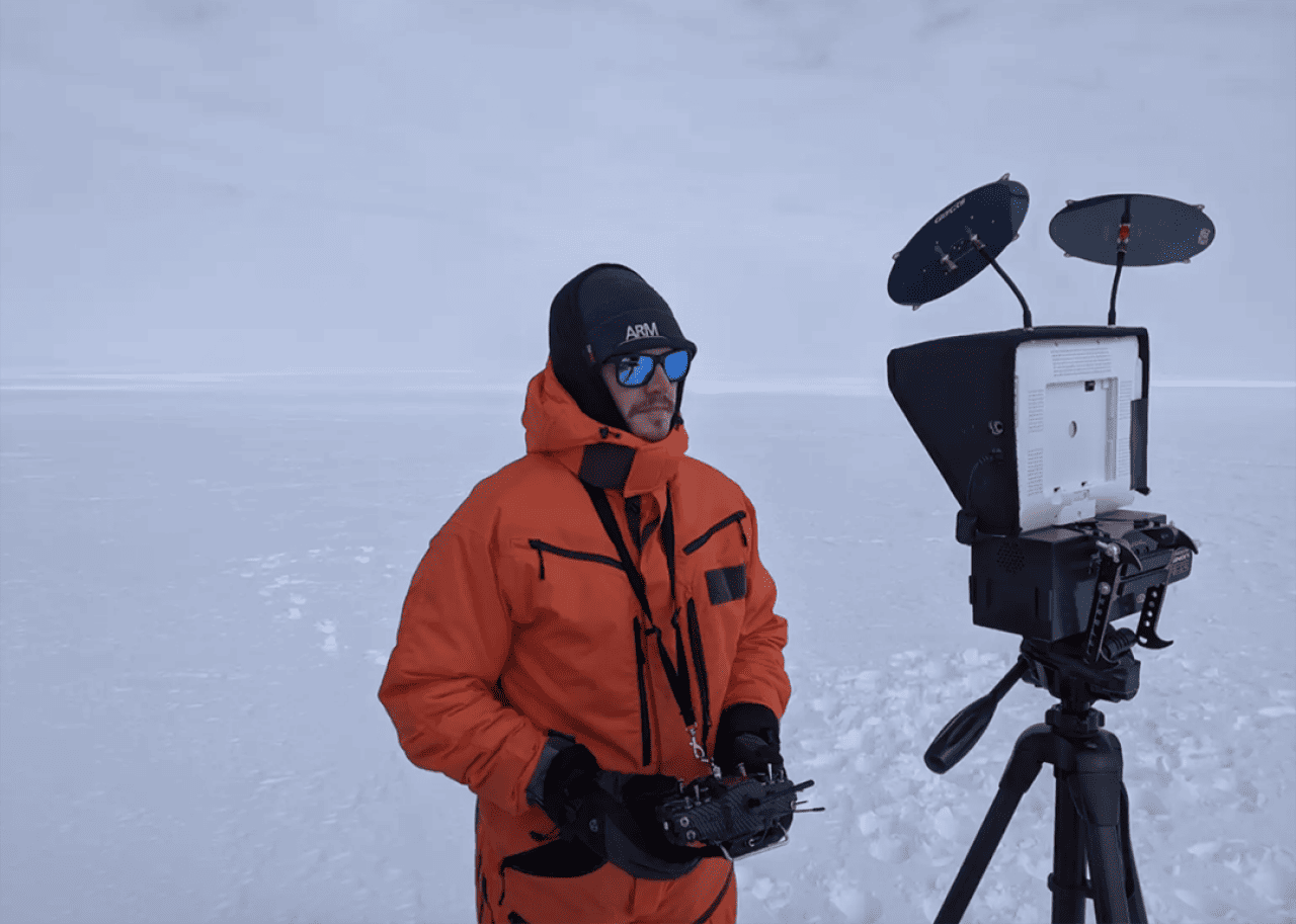 Matthew Boyer in an orange jacket pilots a data-collecting drone while standing on a sheet of ice and snow.