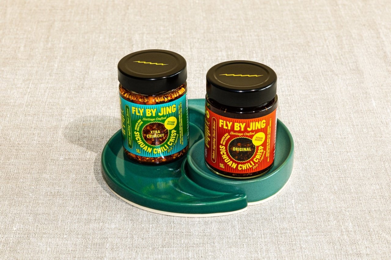 Two jars of Fly By Jing chili crisp sitting on a green yin-yang shaped ceramic dish. 