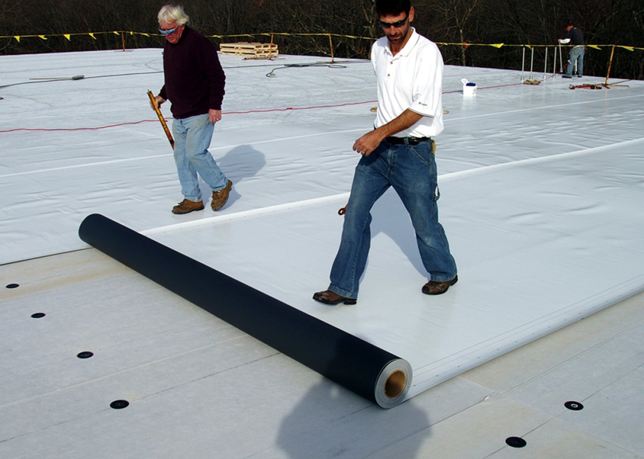 Workers lay down white PVC roofing material on a commercial building in Massachusetts.