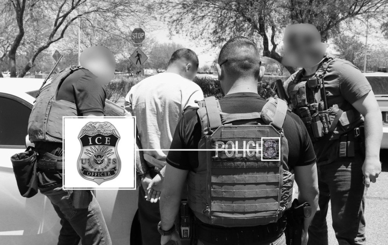 Black and white photo of  group of four U.S. Immigration and Customs Enforcement (ICE) officers, wearing tactical vests and armed with weapons, detain a man in a white shirt with his hands cuffed behind his back next to a car. Enlarged inset shows detail of ICE patch on vest.