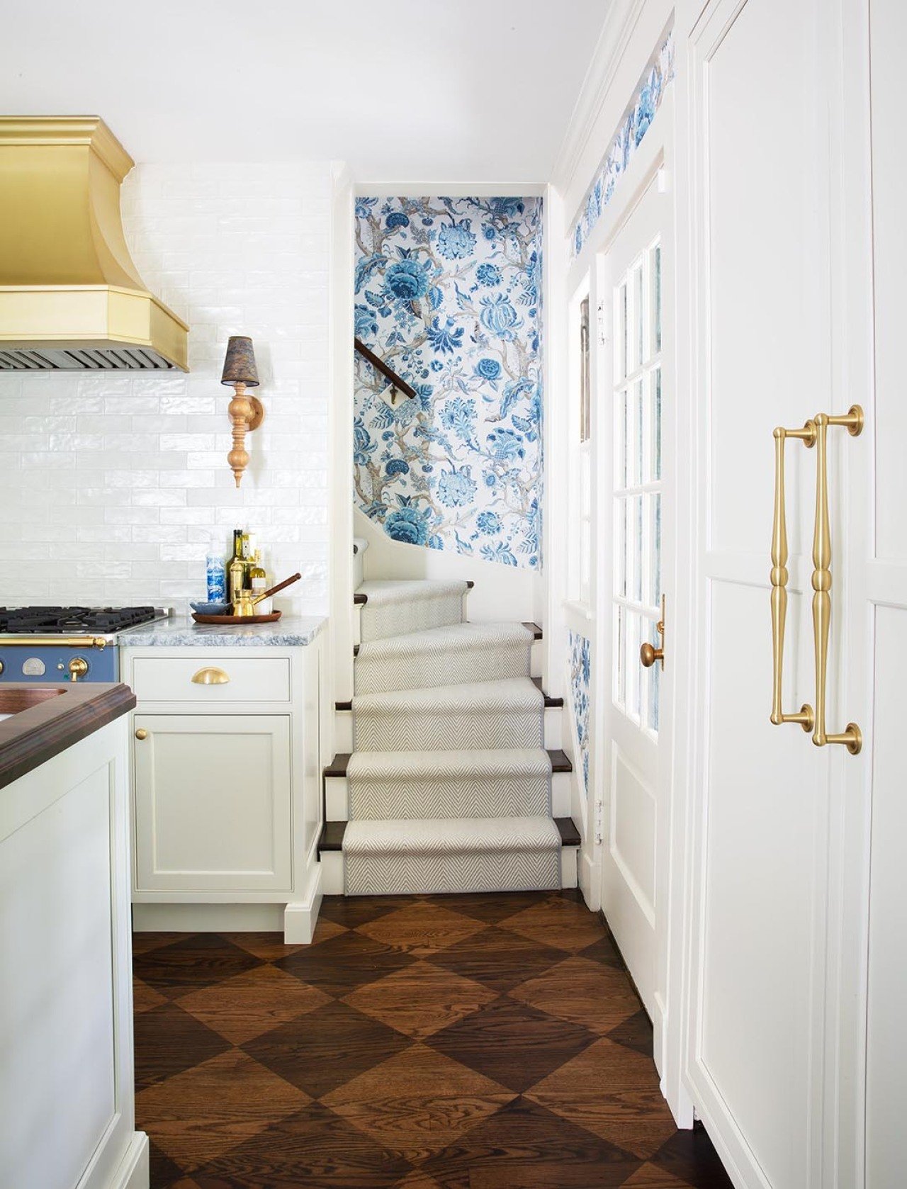 White carpeted stairwell leading out of the kitchen has blue and white wallpaper, patterned wood floor is also visible.