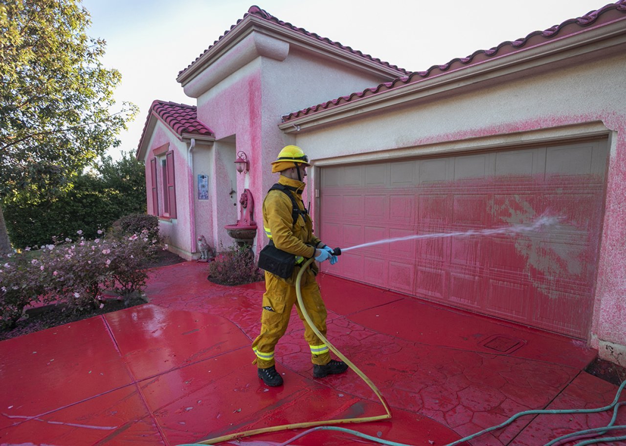 A firefighter cleans Phos-Chek fire retardant from a home.