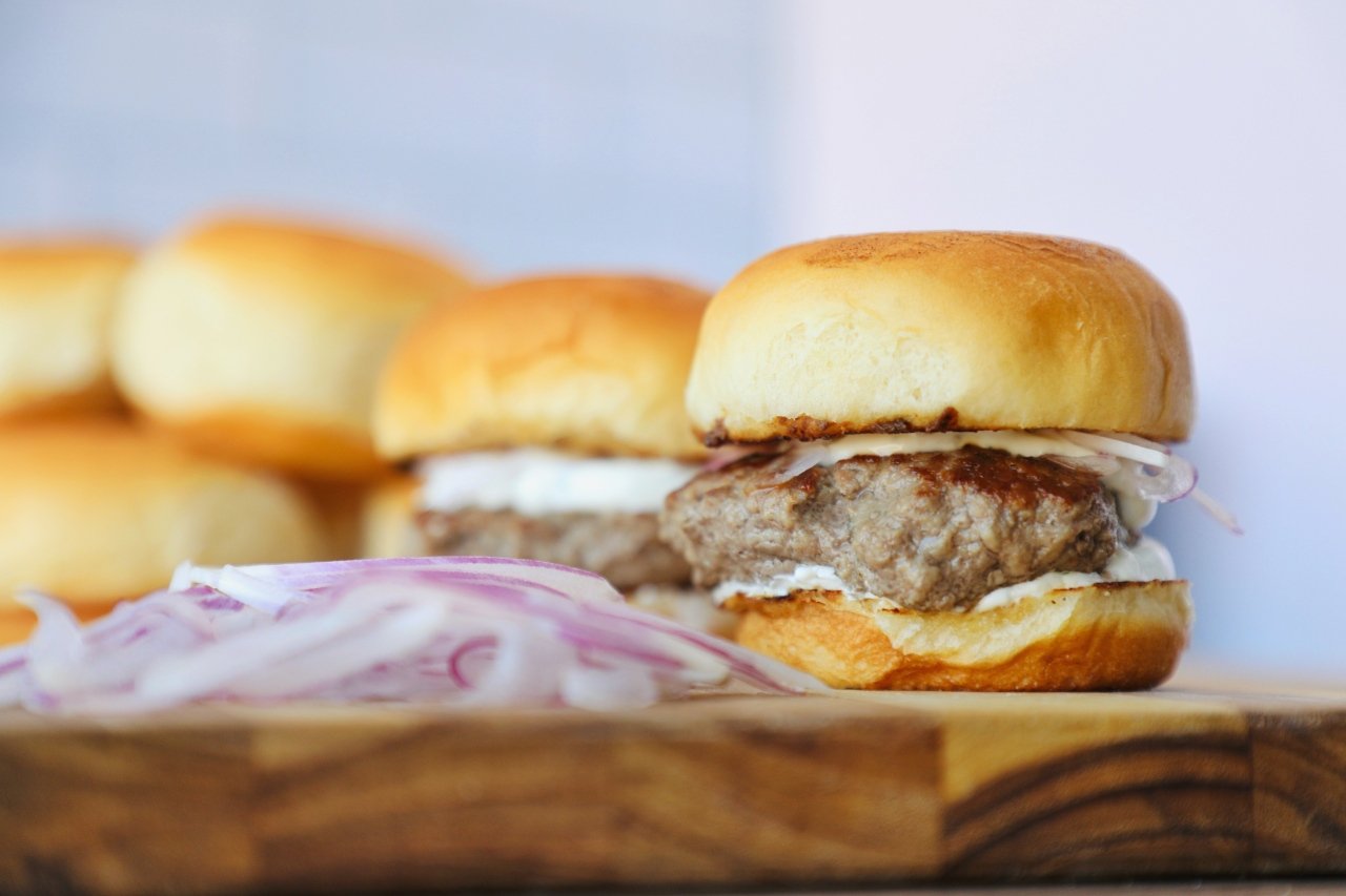 Greek lamb sliders served with raw onions on a chopping board.