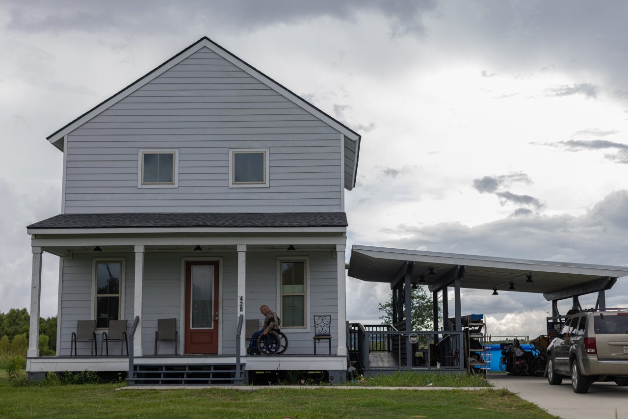 Chris Brunet, pictured here in front of his house, using a wheelchair, in the Louisiana Isle De Jean Charles resettlement, known as “The New Isle.” Brunet was one of the 37 people or families in the first fully federally-funded relocation project in the country.
