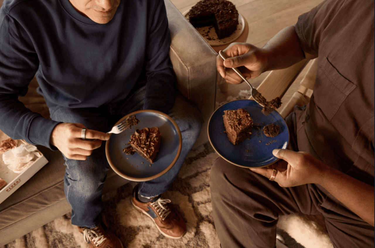 Top down view of two people eating chocolate cake on blue plates. They are wearing Oura rings on their index fingers. 