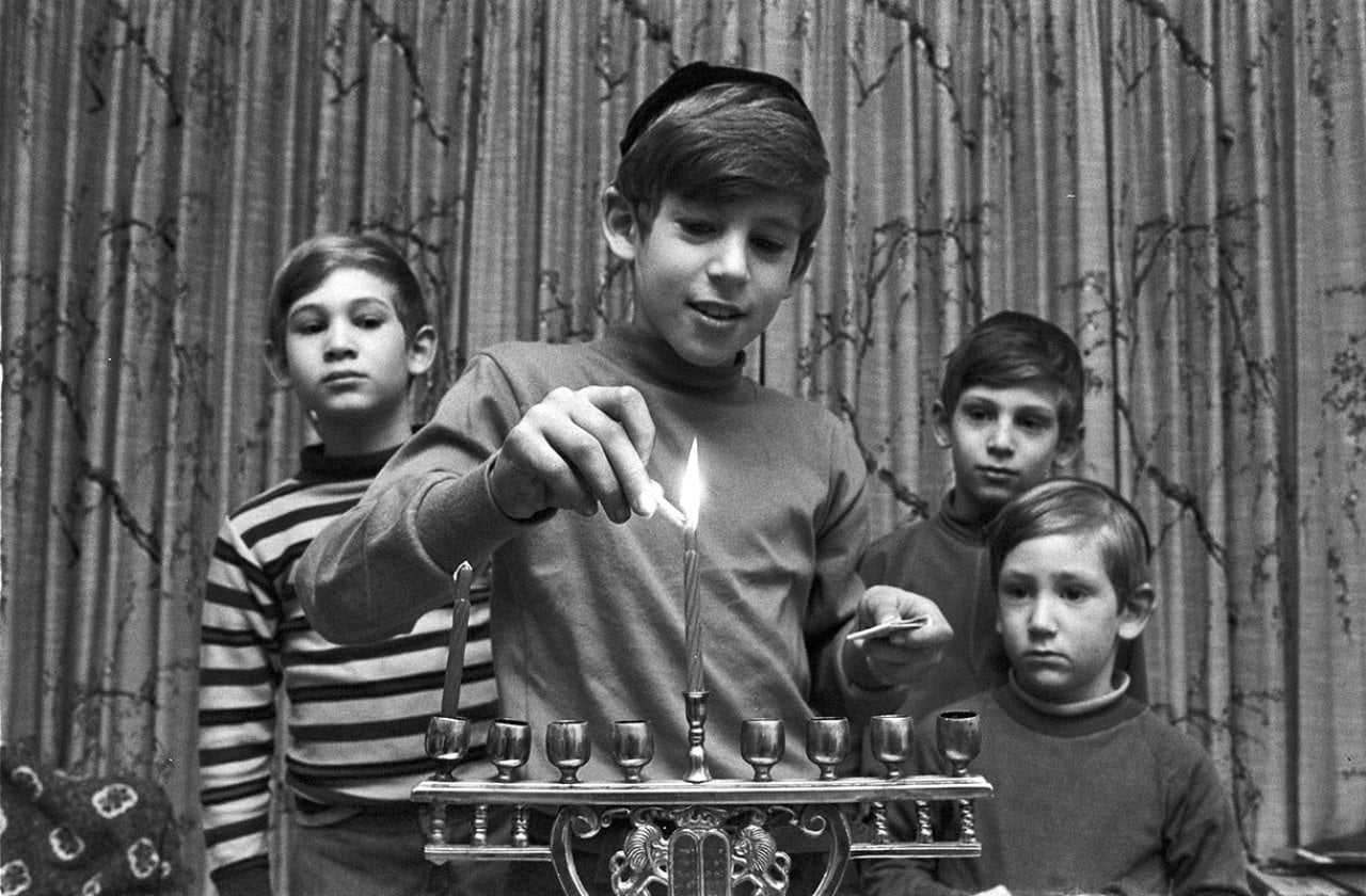 Black-and-white photo four boys of a Jewish family lighting a menorah during Hanukkah, Brookline, Massachusetts, 1971.