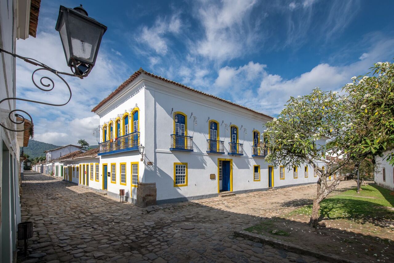 View of the exterior of Sandi Hotel, a charming white building on a cobblestone street, with blue sky and clouds above.