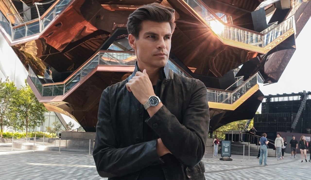 A man posed in front of a building, sporting a casual everyday watch.