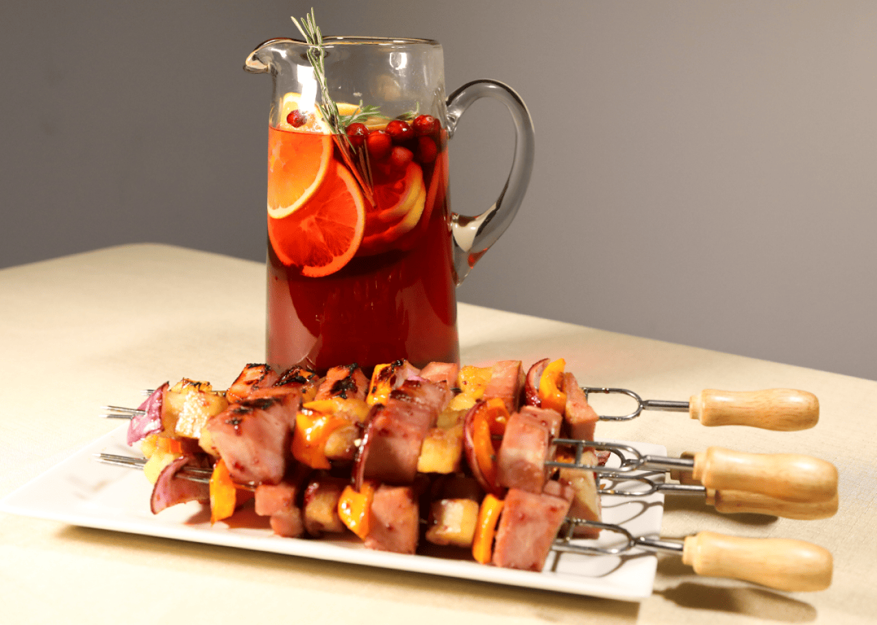 A plate of Holiday Ham Skewers with a pitcher of Jingle Juice Sparkling Sangria.