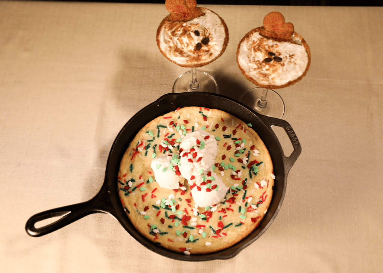 A 'Winter Wonderland' Sugar Cookie on a skillet with two glasses of Gingerbread Espresso Martini.