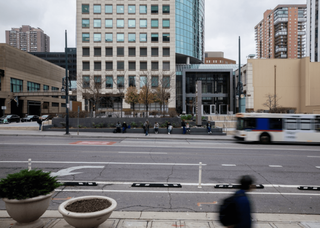 Slow-shutter exposure of a street in Denver with a pedestrian and bus going by and buildings in the background.
