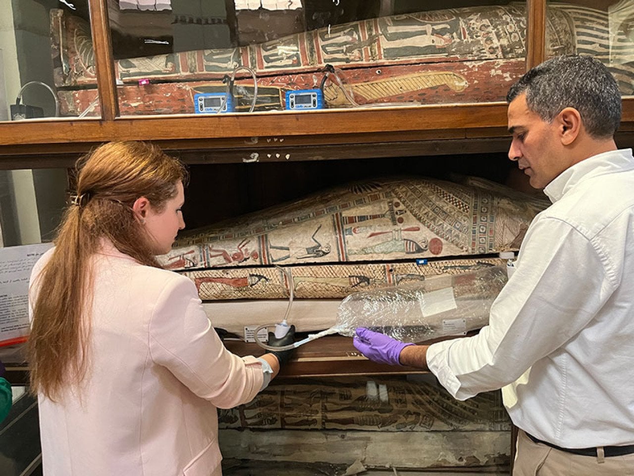 Two scientists wearing gloves and holding a device with tubing and a bag analyizing air next to mummies at the Egyptian Museum in Cairo so they can recreate their scent &mdash; and shed light on the embalming ingredients used to preserve them.