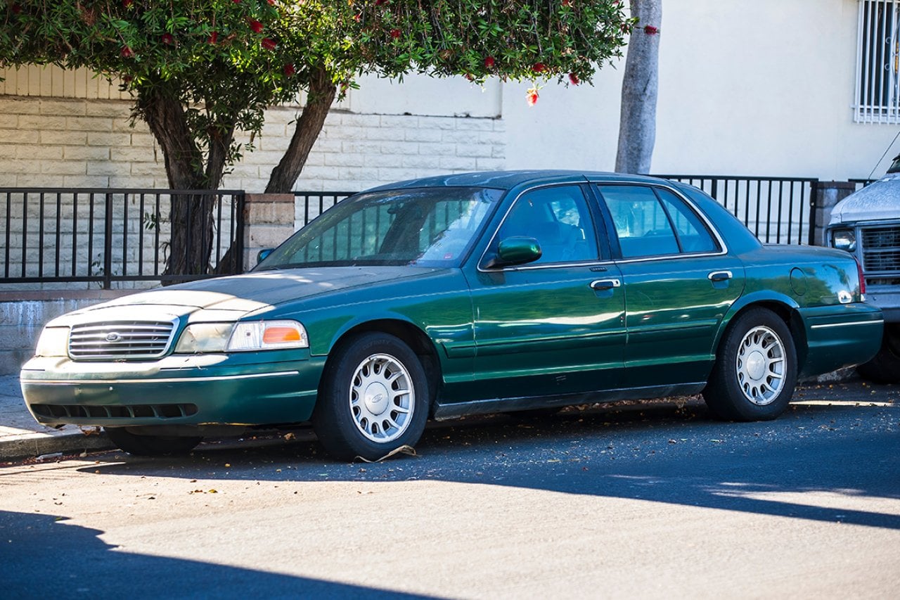 A green Ford Crown Victoria car parked on roadside.