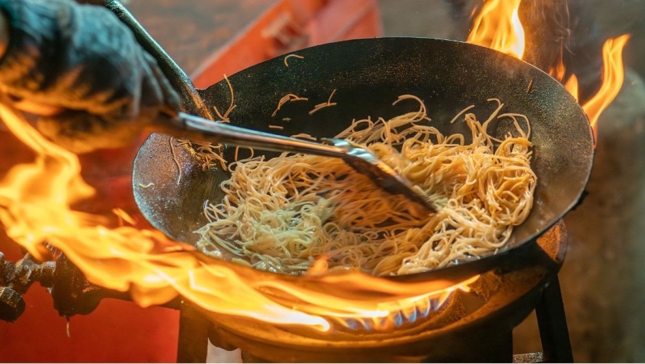 Noodles being cooked in a fiery wok for a Pad Thai dish.