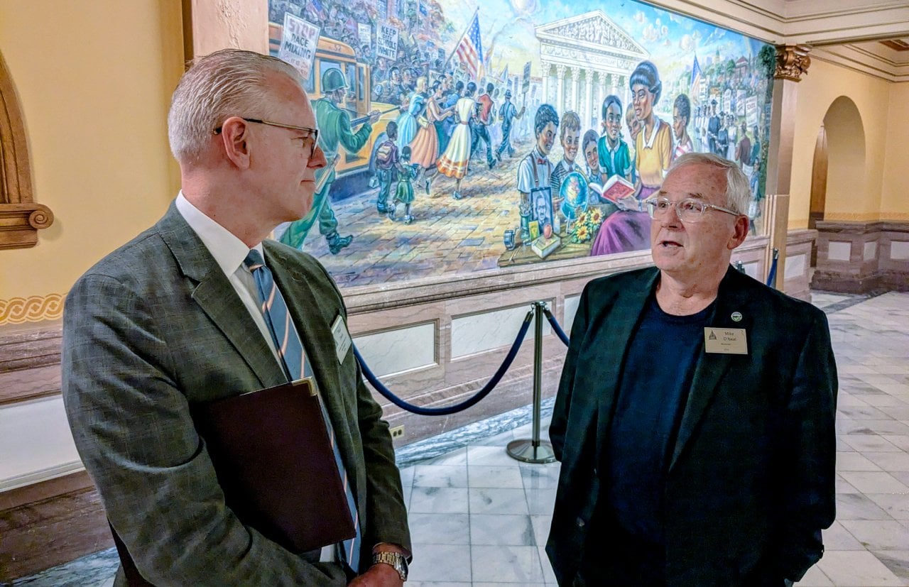 Former House Minority Leader Paul Davis, left, and former House Speaker Mike O’Neal of the Kansas Legislature talking to each other, a mural is visible behind them.