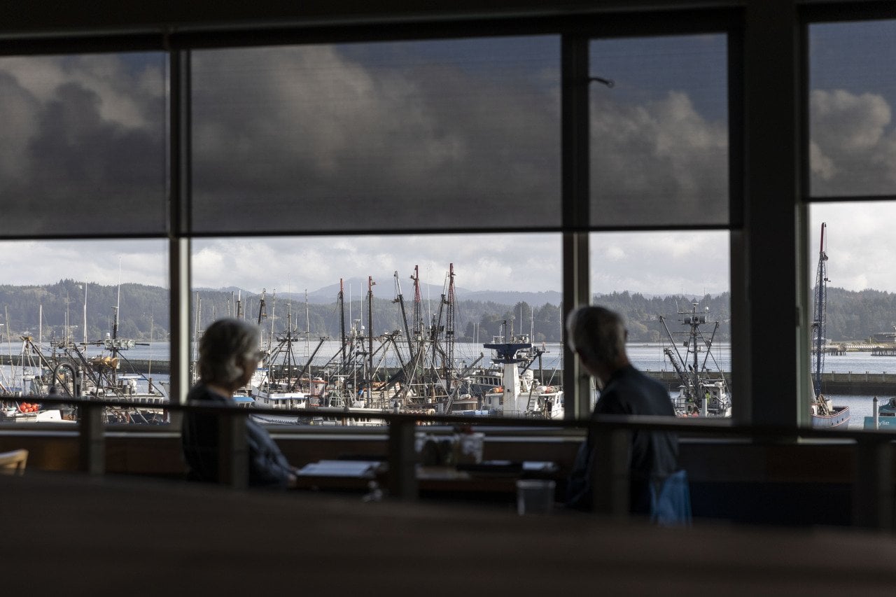 Diners inside a restaurant with a view of the ocean just outside the window.
