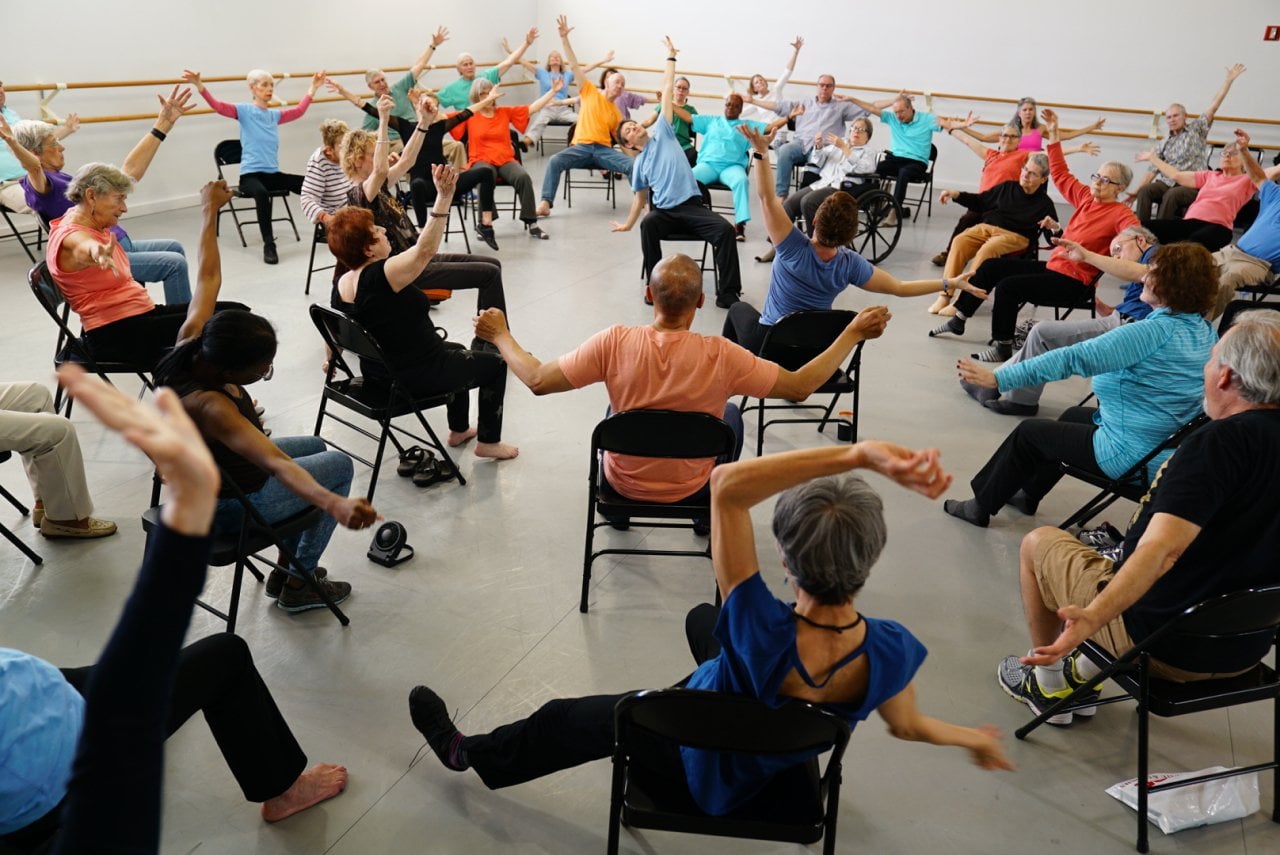 High-angle view of a room full of people dancing while in folding chairs.