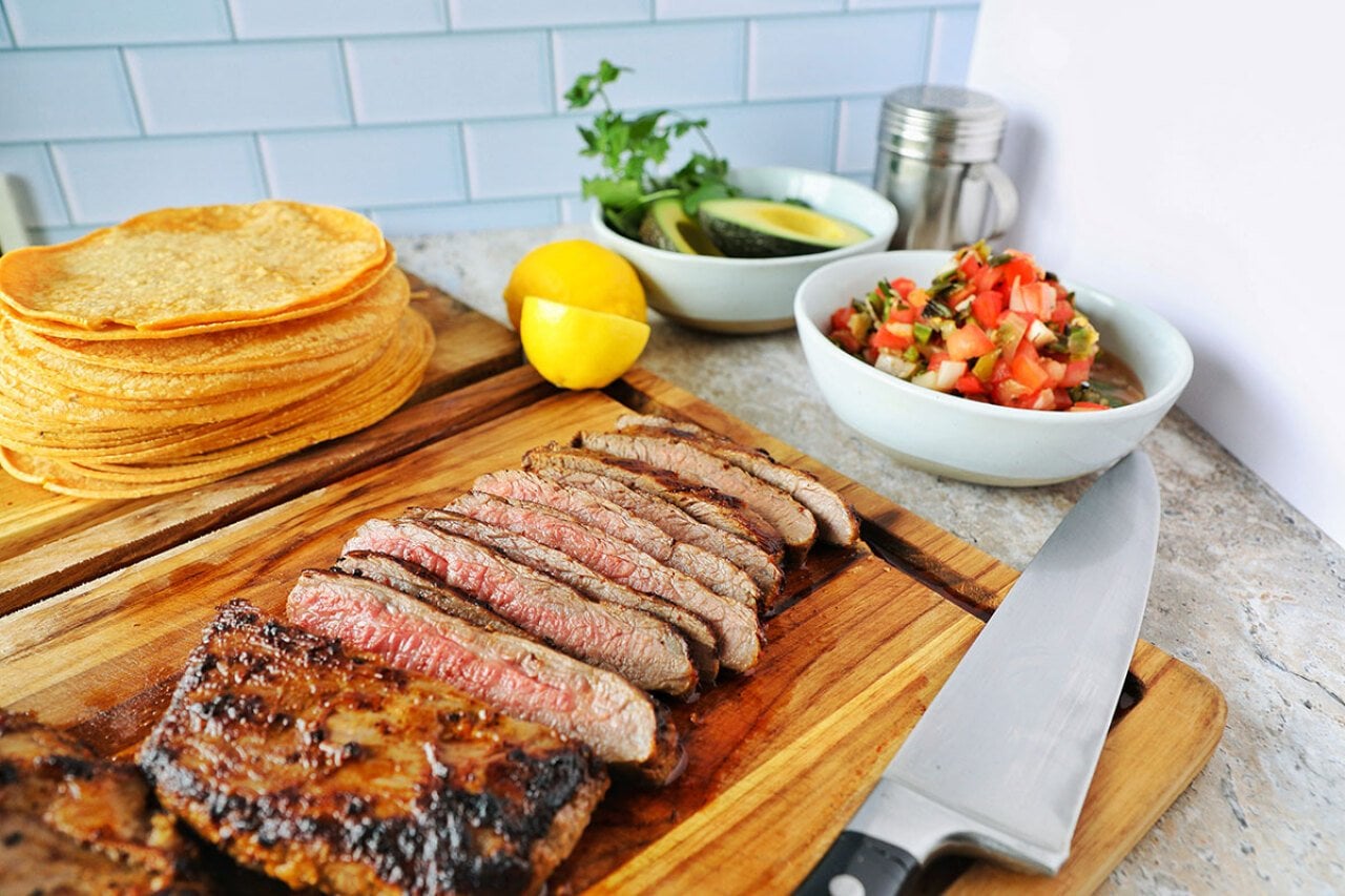 A plate of sliced carne asada with salsa and tortillas on the side.