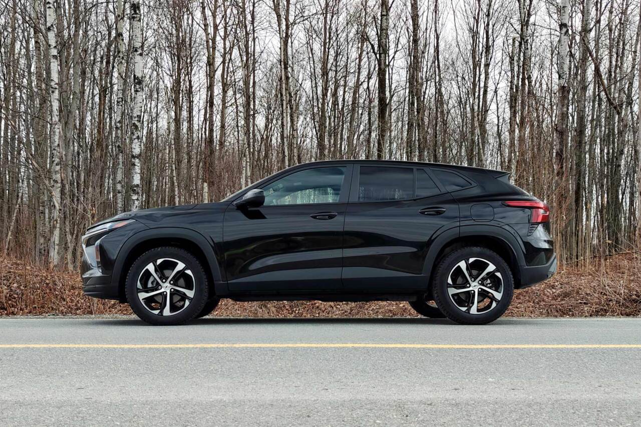 Side view of black 2026 Chevrolet Trax parked on road in front of bare trees.