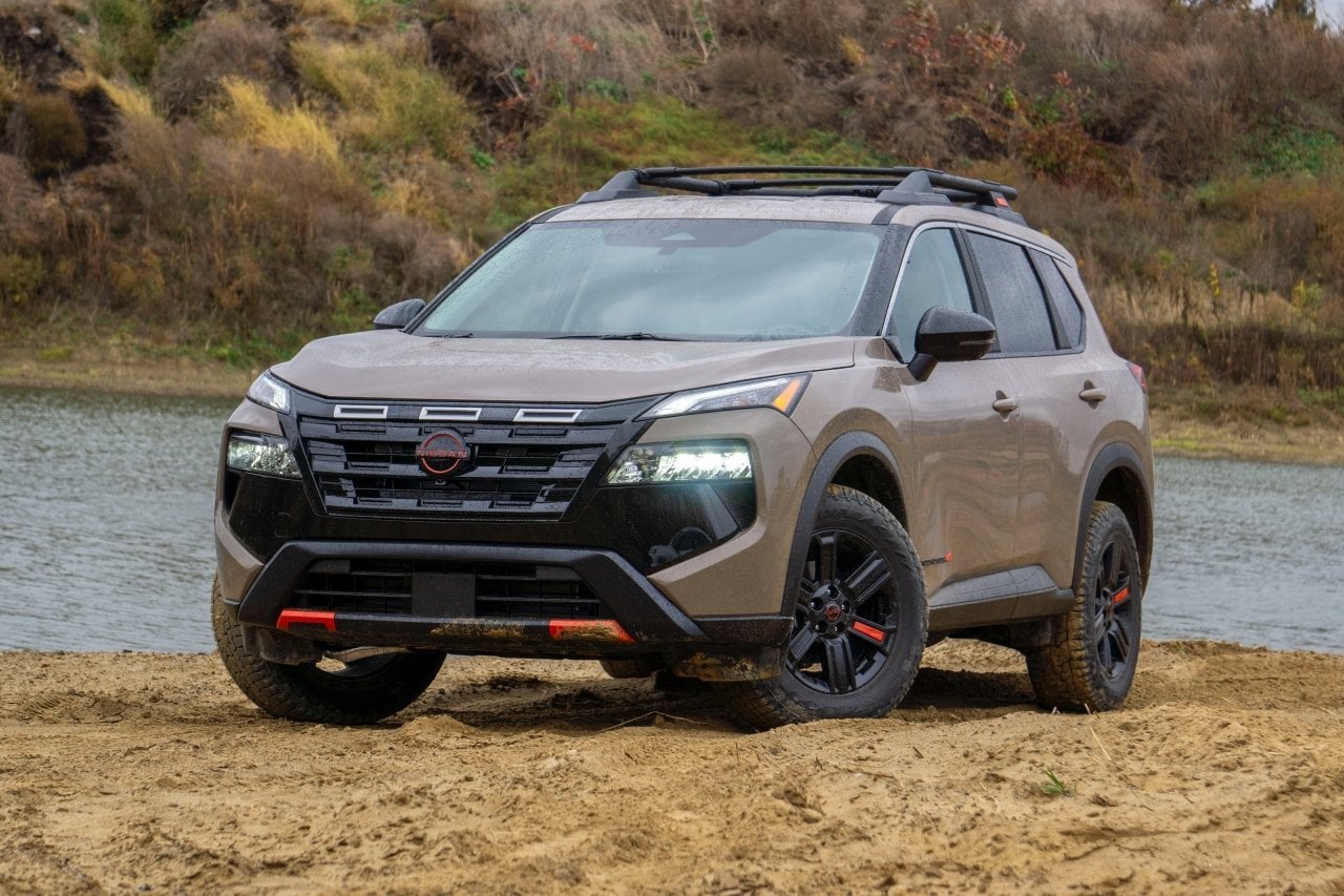 Front low-angle view of a light brown 2025 Nissan Rogue parked on the sandy banks of a river.