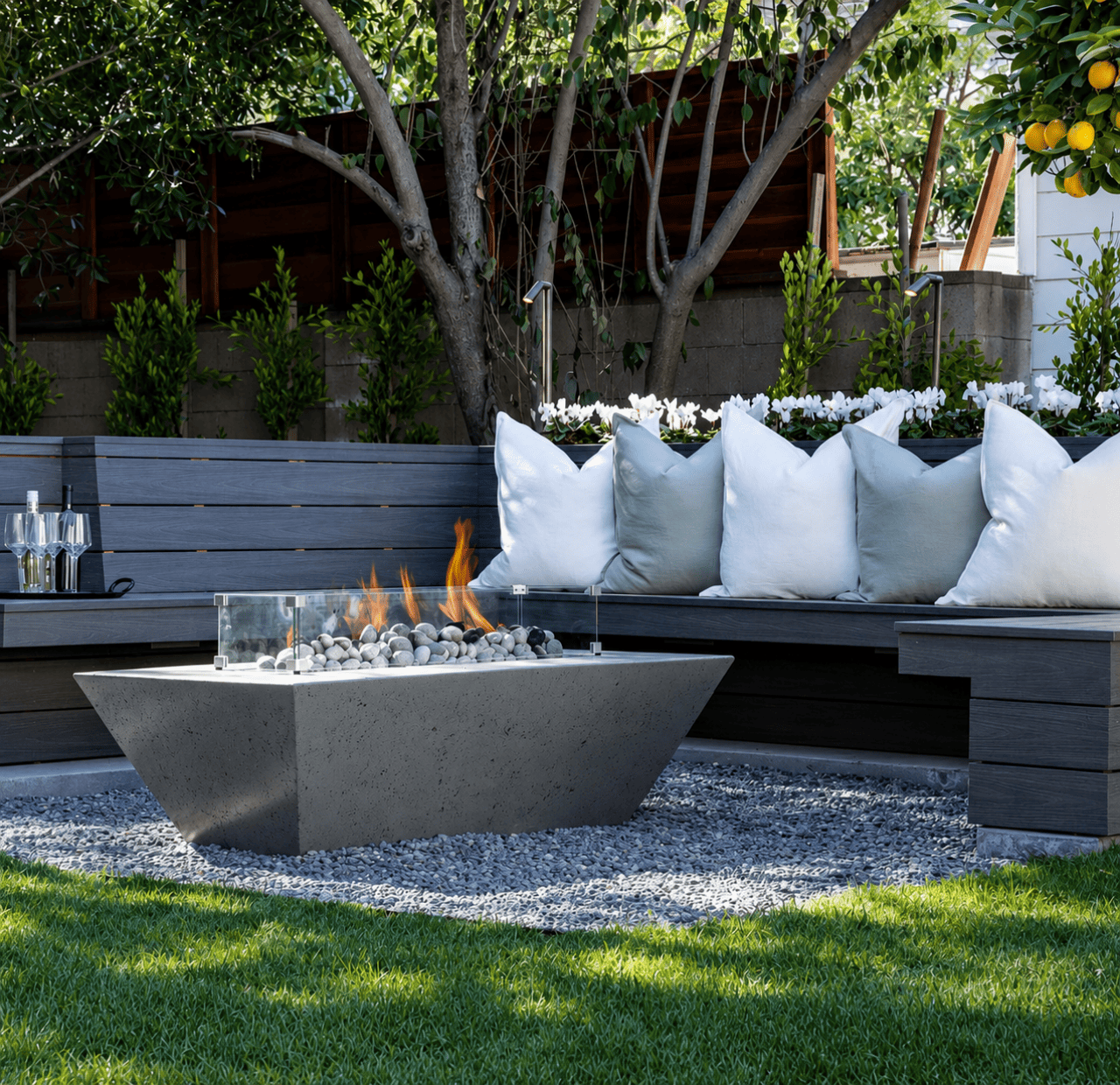 An outdoor space featuring a centerpiece rectangular gas fire pit table with concrete and glass finishes.