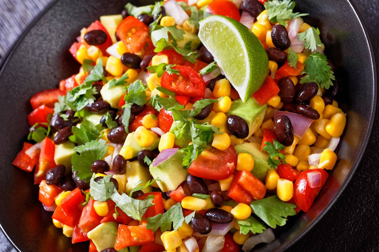 Santa Fe grilled corn salad garnished with lime and fresh cilantro leaves in a plating dish.