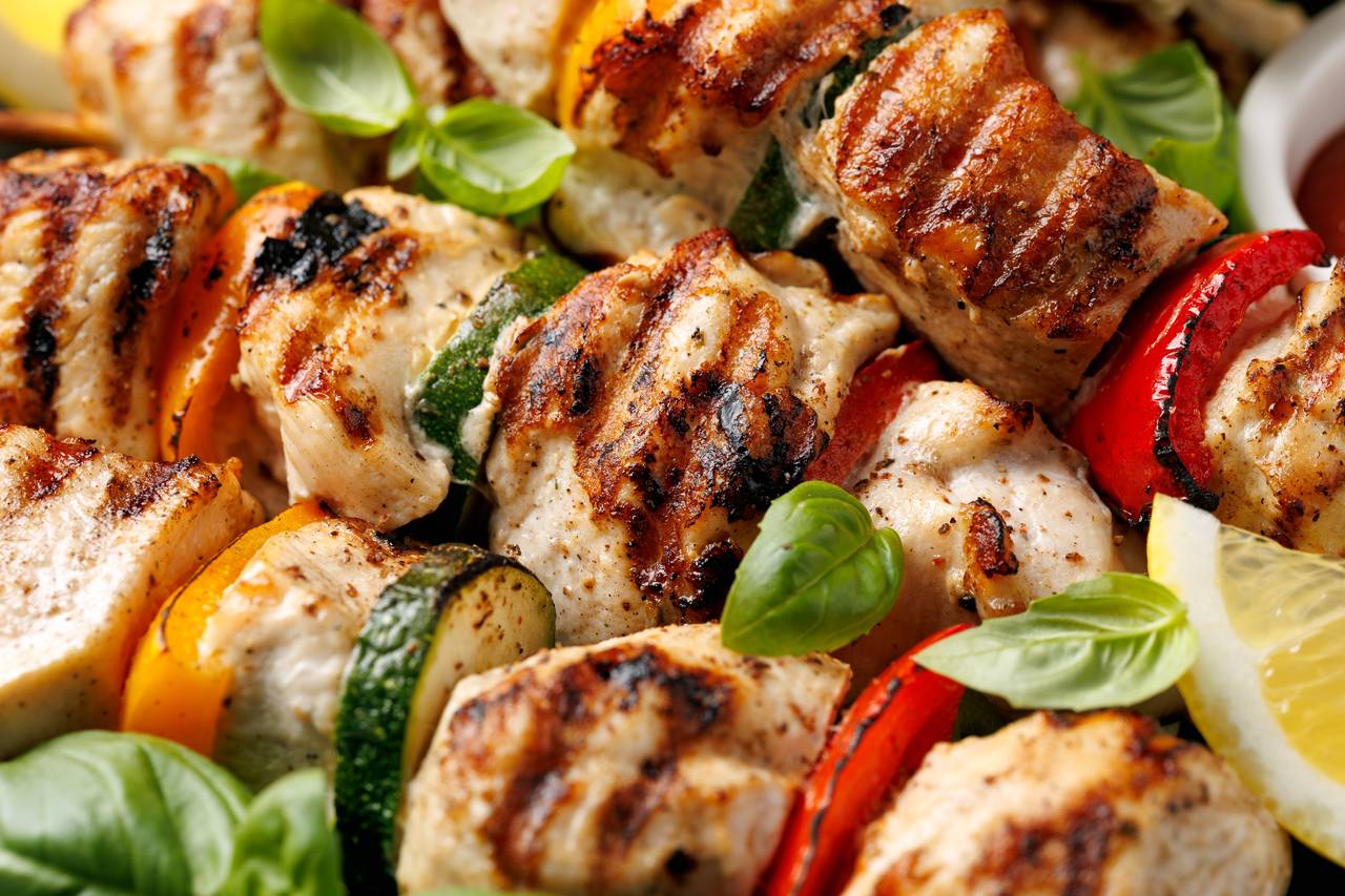 Lemon herb chicken skewers with zucchini, bell peppers, red onions, and basil leaves served in a plating dish.