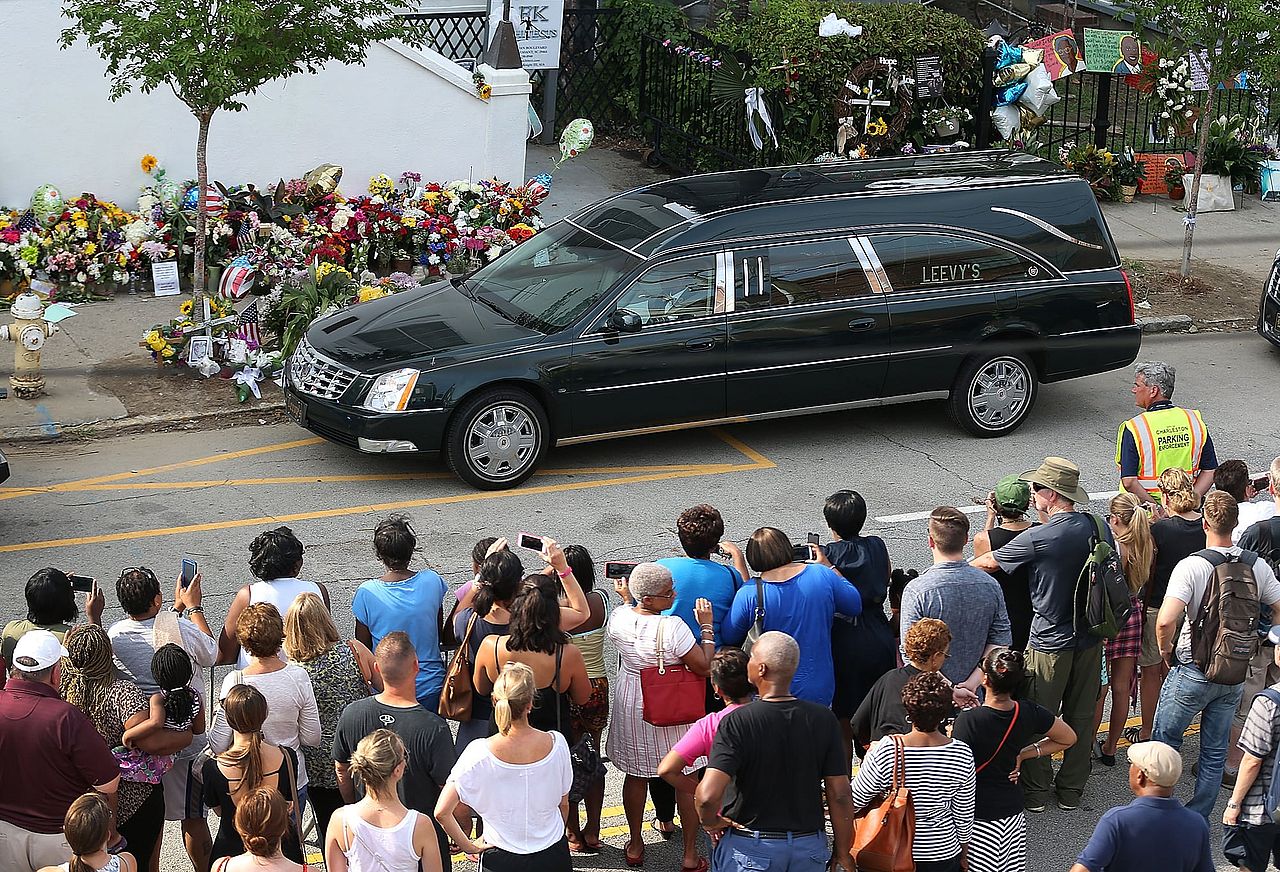 People watch as a hearse carrying the casket of Sen. Clementa Pinckney passes Emanuel AME Church in Charleston, SC.