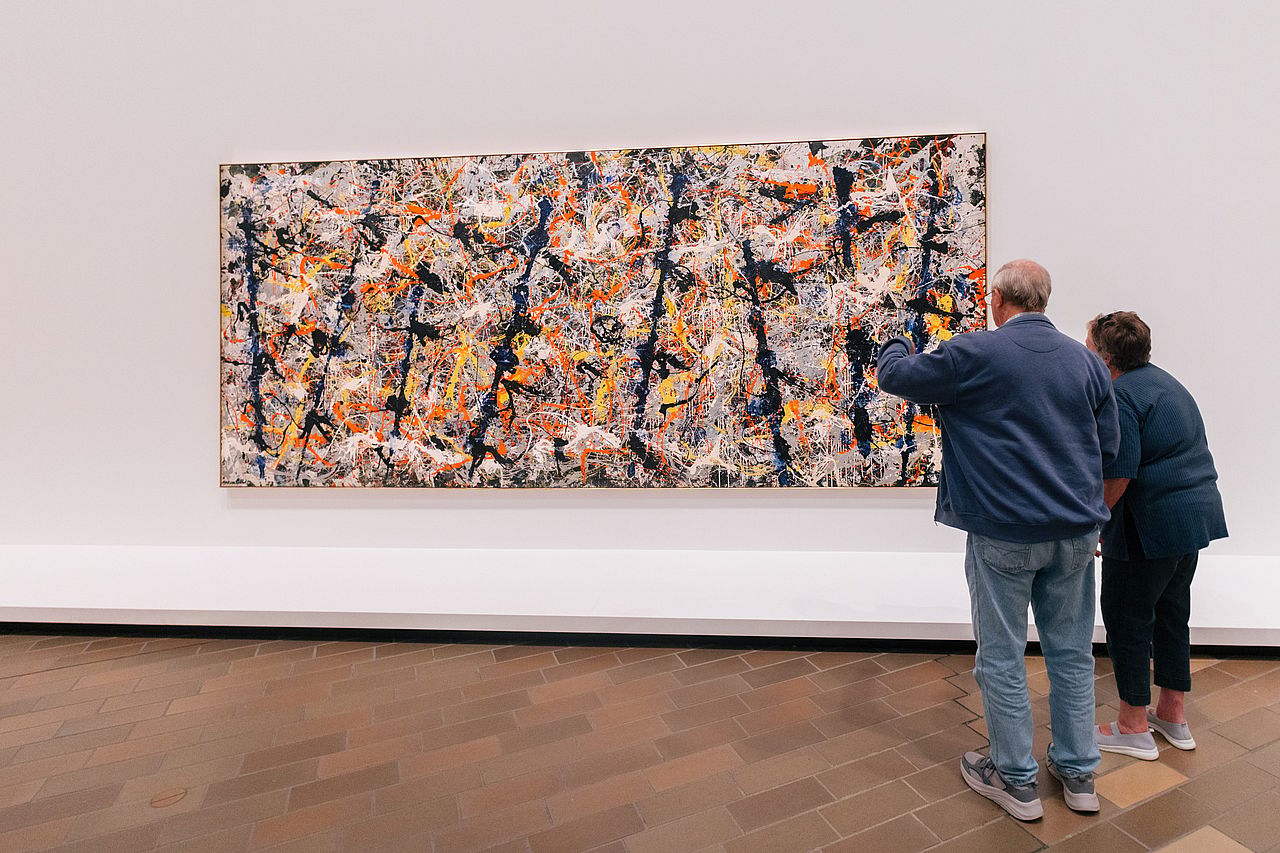 Two people looking at a wide abstract painting on a white wall at the National Gallery of Australia.