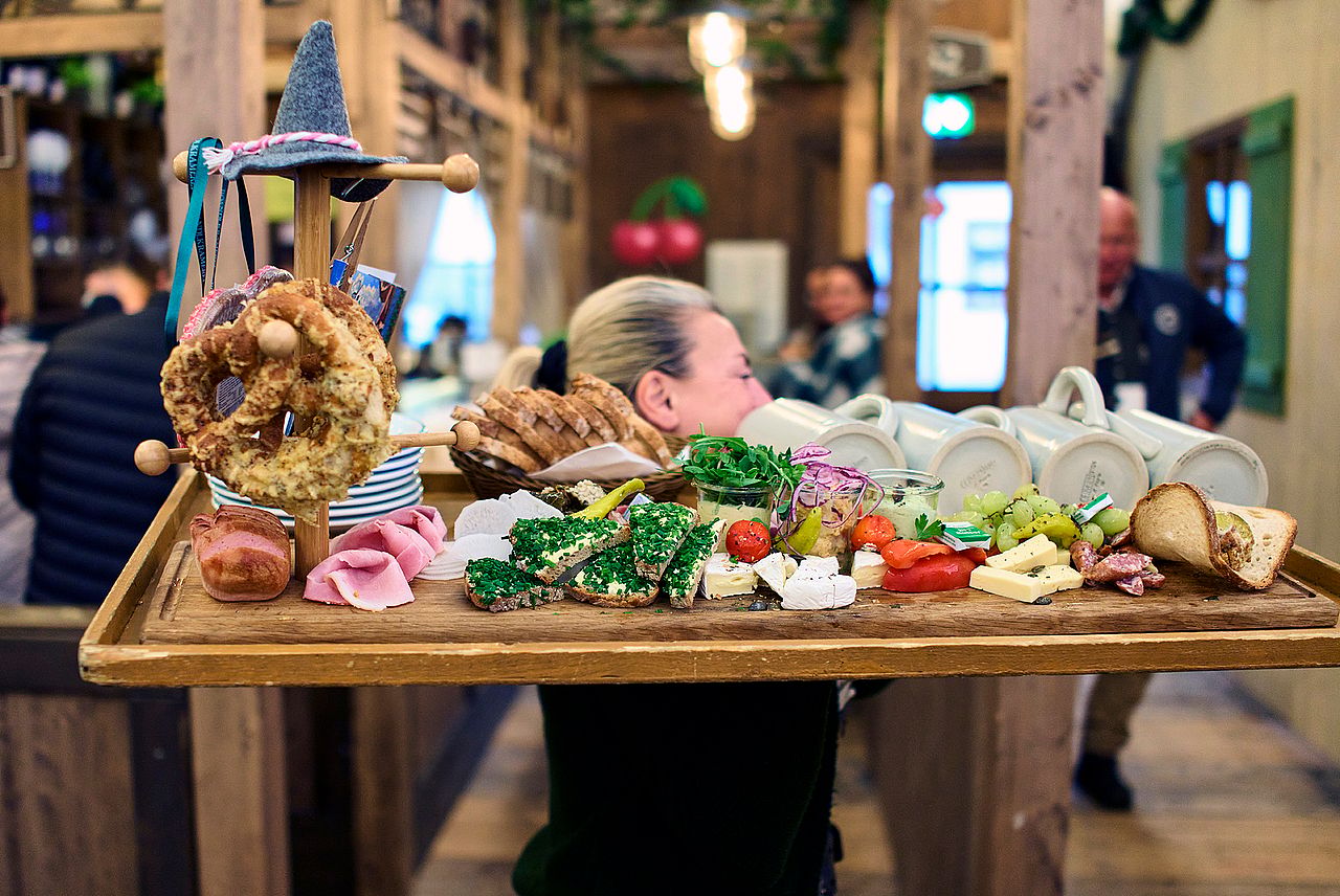 A waitress carries a wooden board with cheeses, breads, vegetables, and fresh garnishes during the final day of Oktoberfest festival on October 5, 2025 in Munich, Germany.