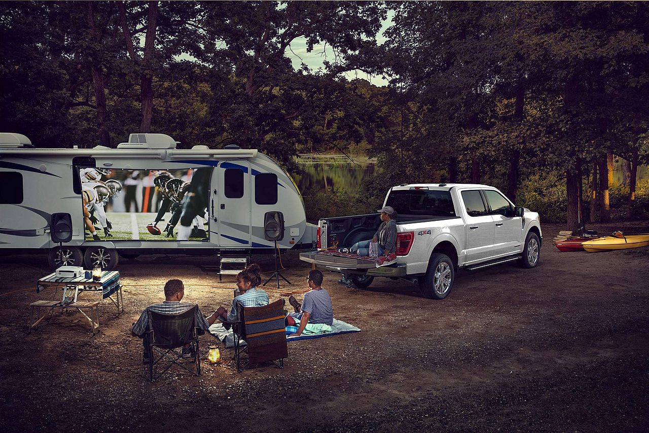A 2024 Ford F-150 powers an entire campsite with its Pro Power Onboard feature, with people gathered to watch a football game.