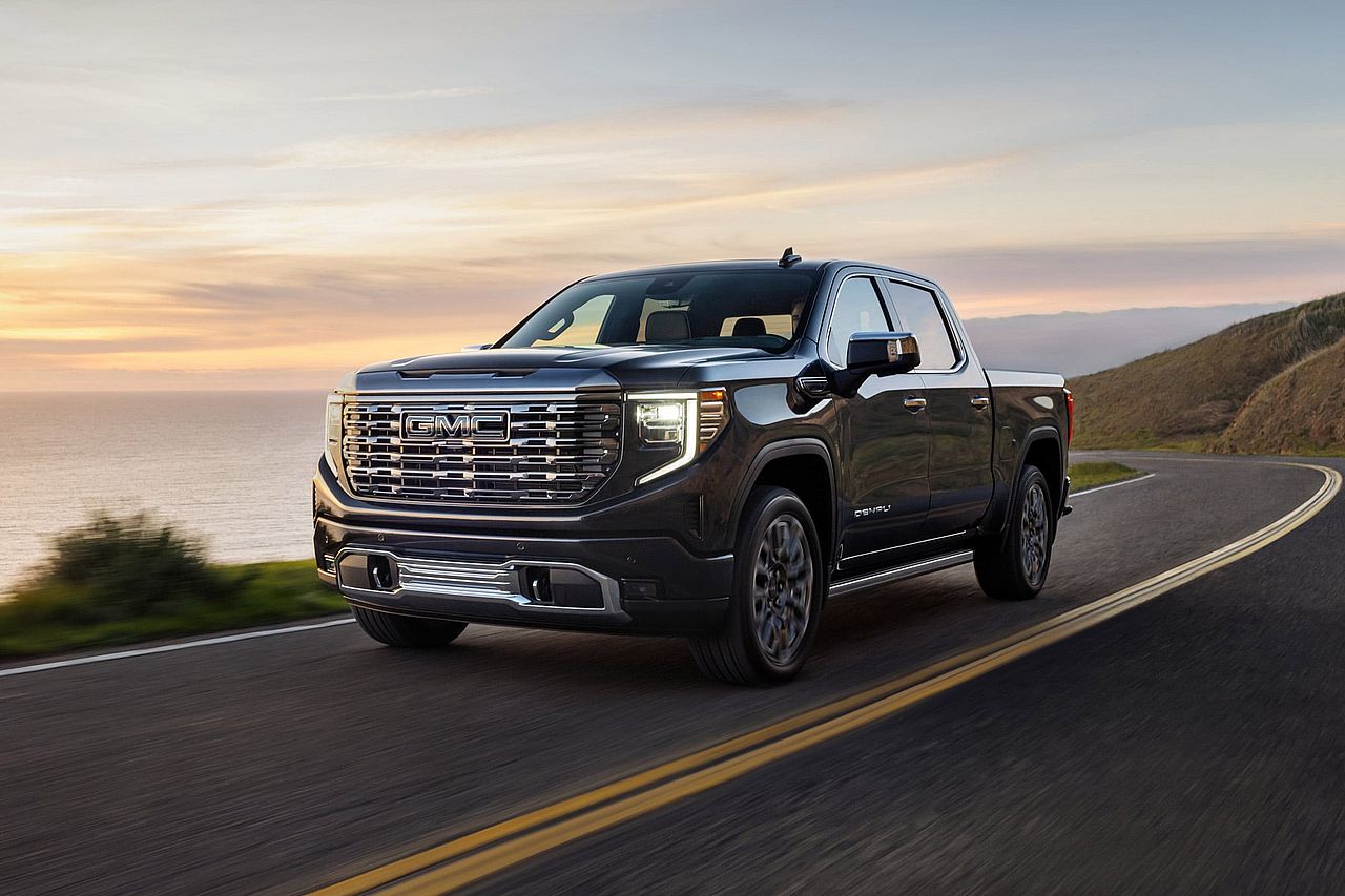 2026 GMC Sierra 1500 Denali Ultimate in Onyx Black, driving on a coastal highway at sunset.