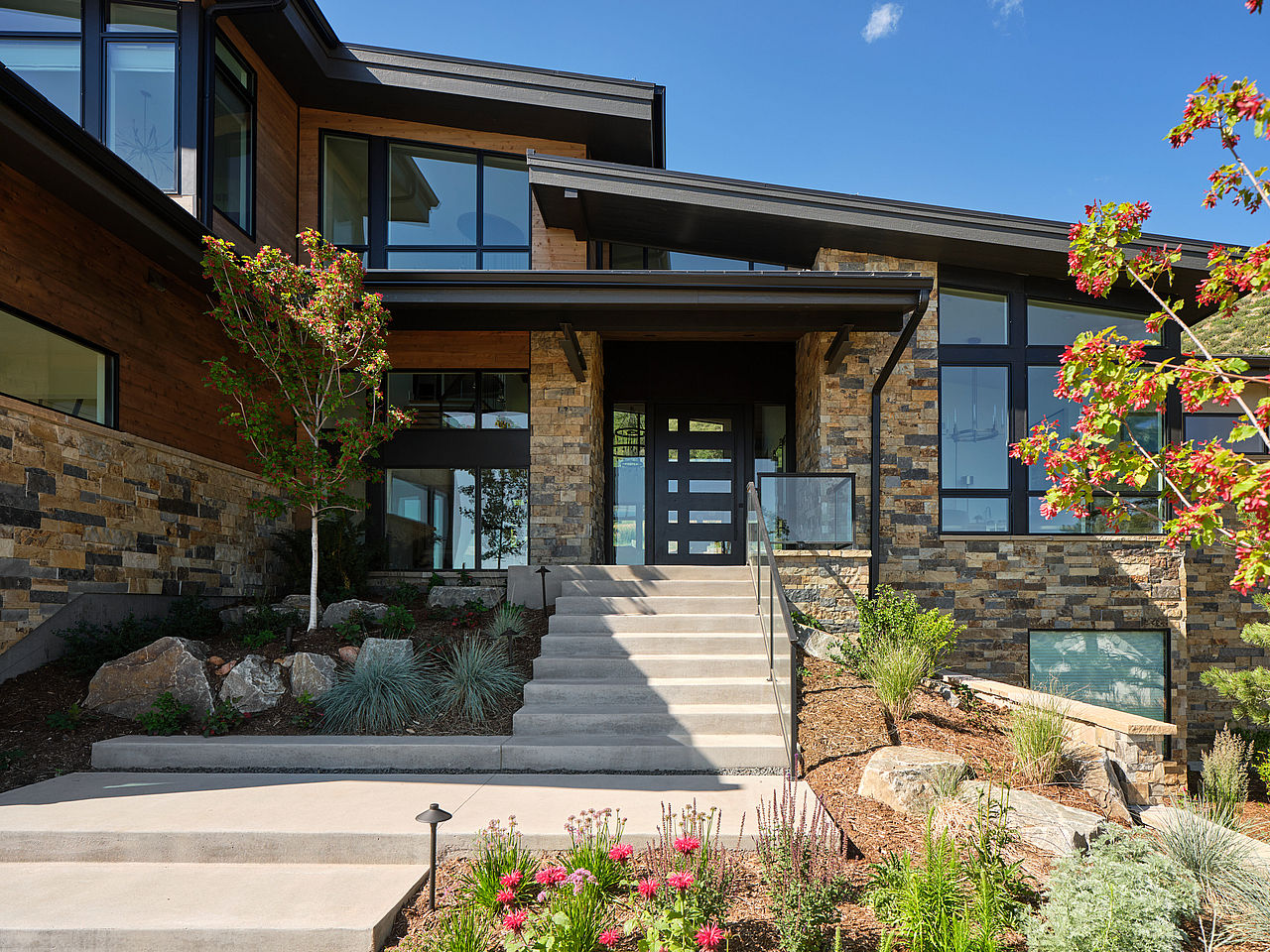 Exterior of home with stonework, large windows and modern black roofs.