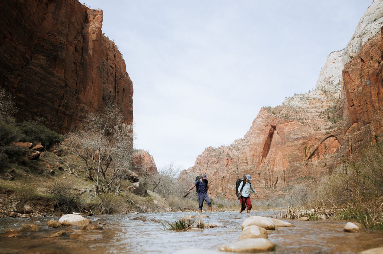 A pair of hikers cross a stream of water during a trail.