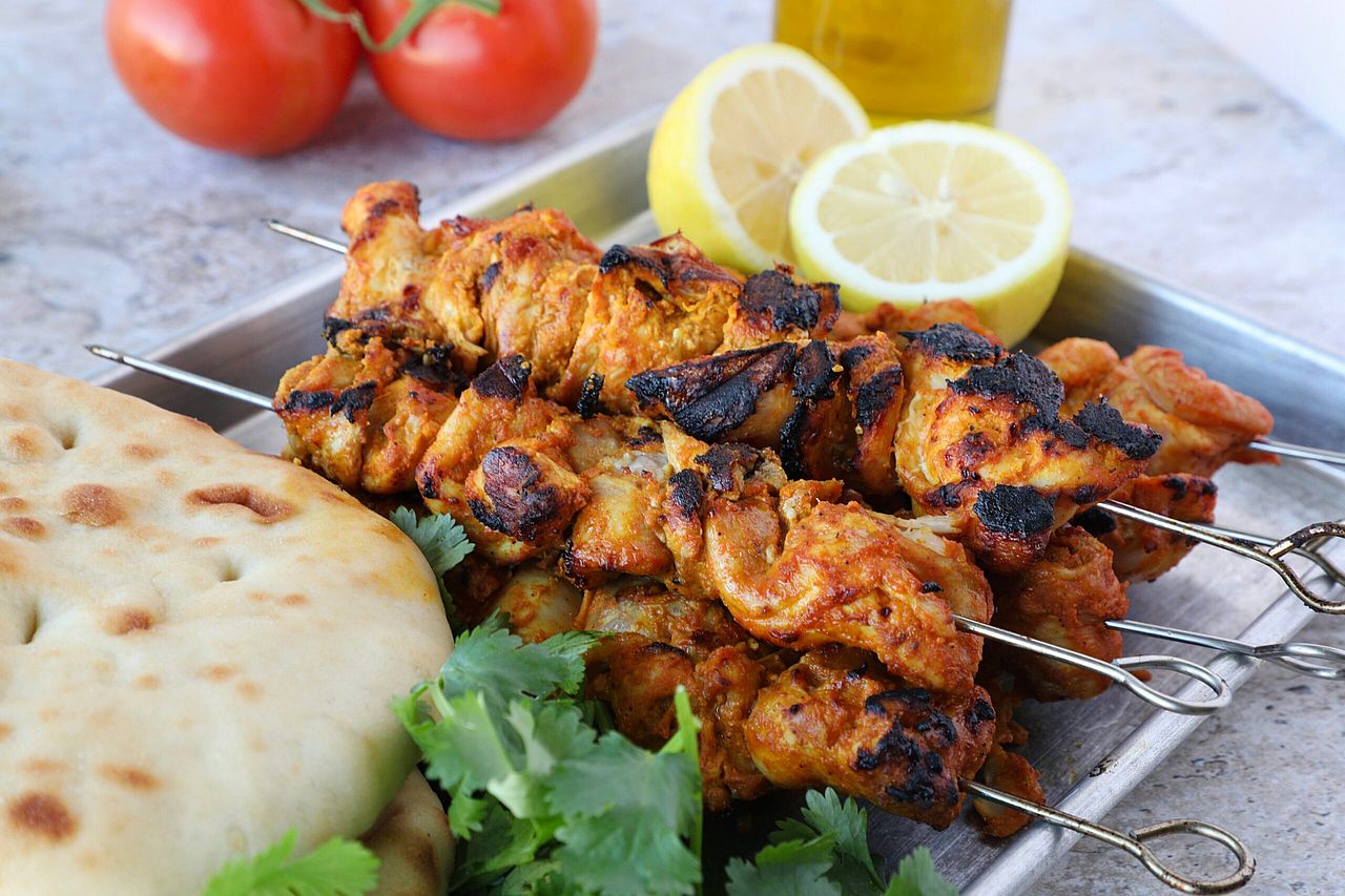 A dish full of chicken tikka skewers served with flatbread, fresh cilantro, and lemon wedges.
