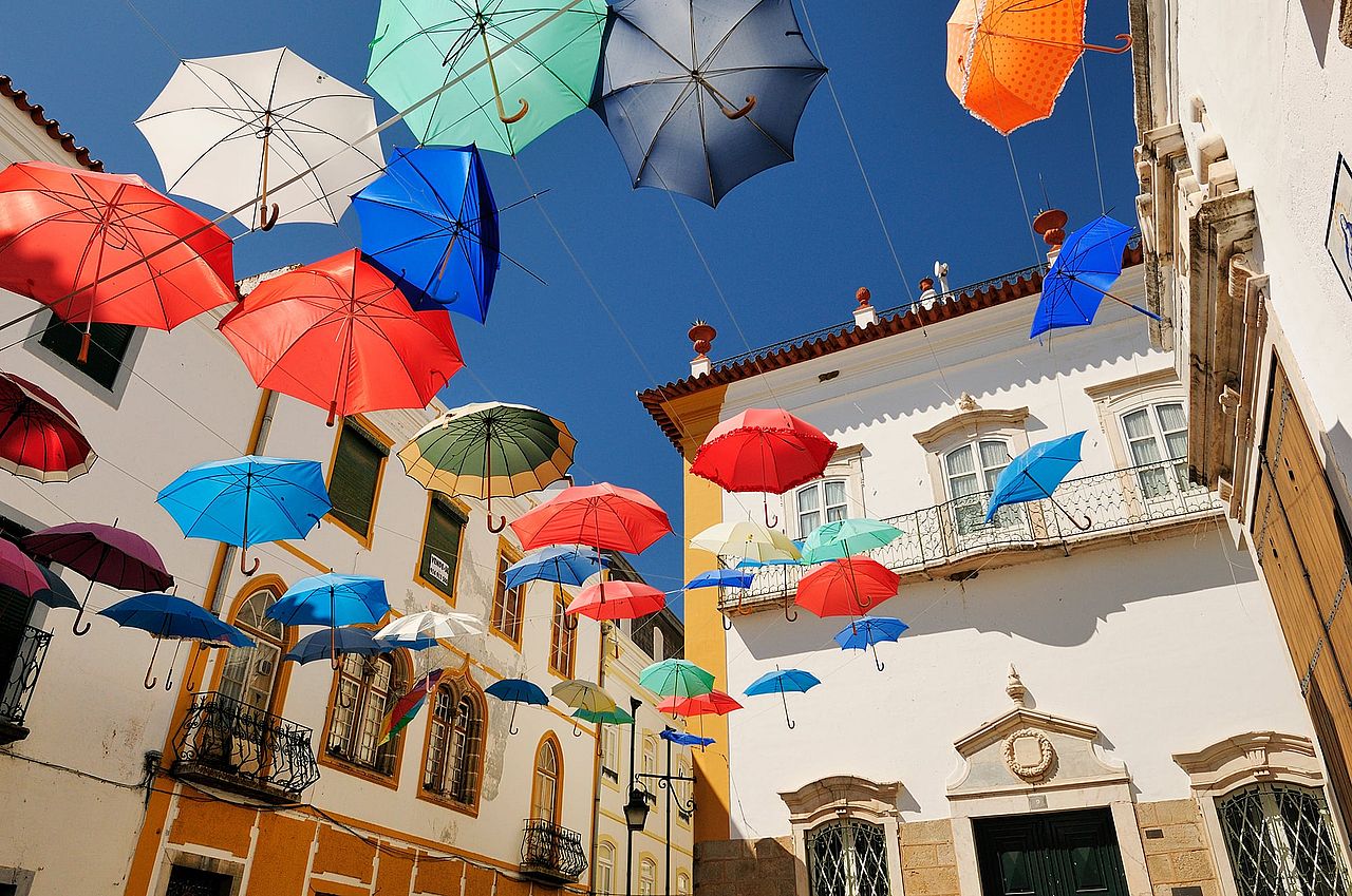 A public square decorated with an installation of floating colorful umbrellas in Évora, Portugal.