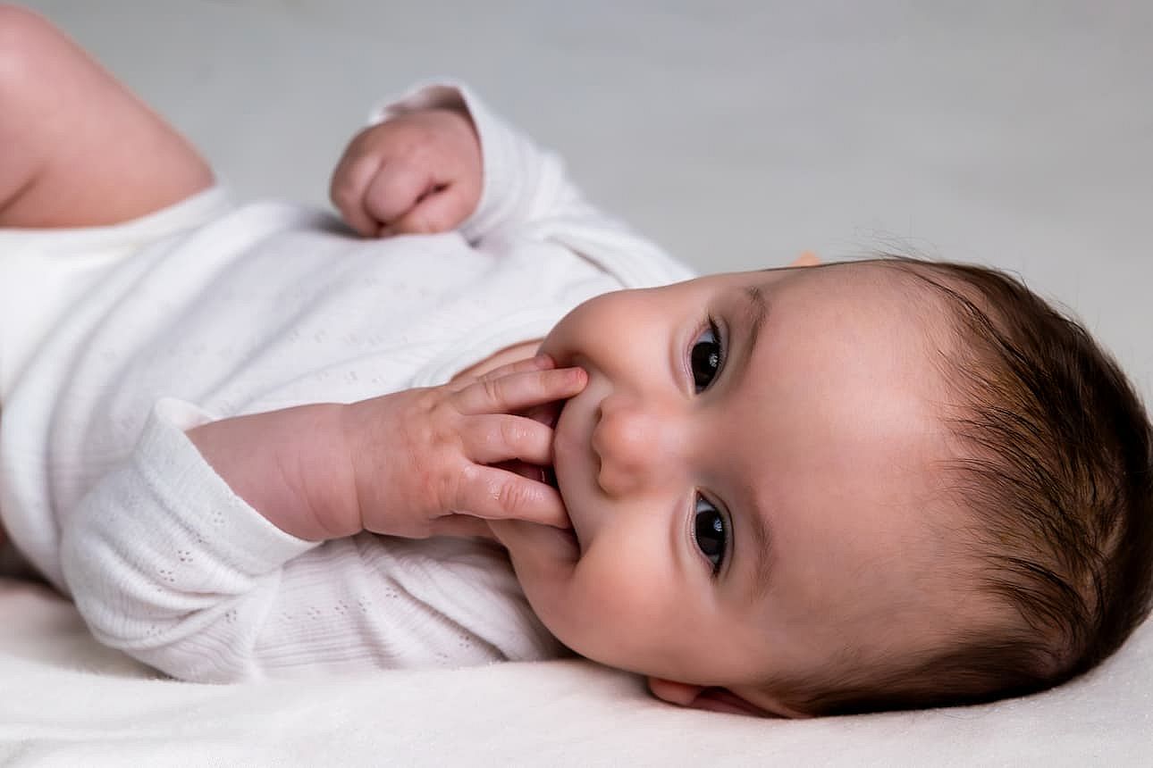 Baby infant lying on back innocently sucking fingers